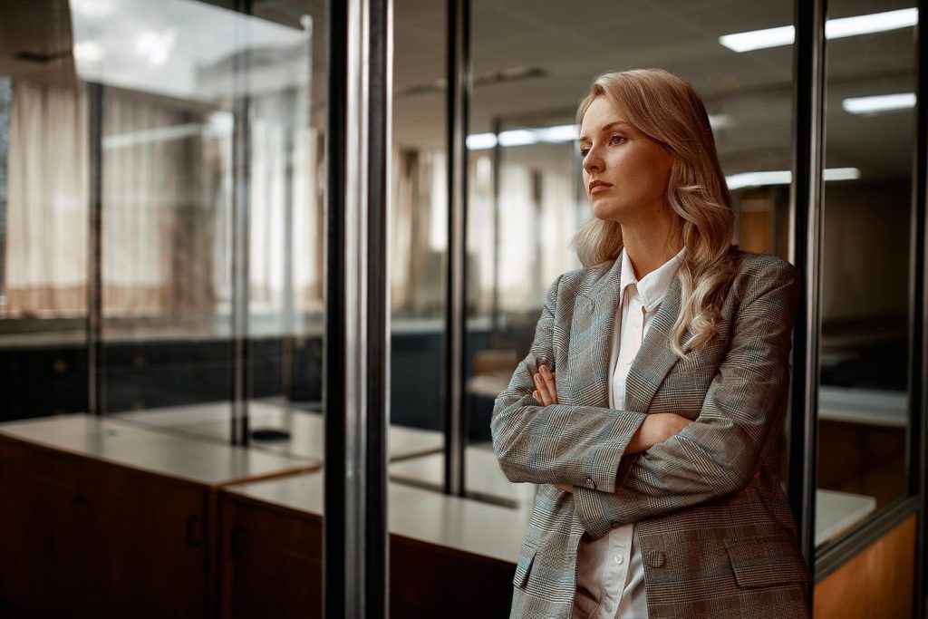 Zdjęcie jest ilustracją do artykułu i przedstawia bizneswoman opartą o ścianę z szyb w open space.