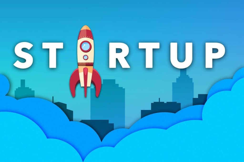 Grafika jest ilustracją do artykułu i przedstawia słowo "startup" na niebieskim tle graficznego miasta. Zamiast litery A w wyrazie "startup" znajduje się rakieta.