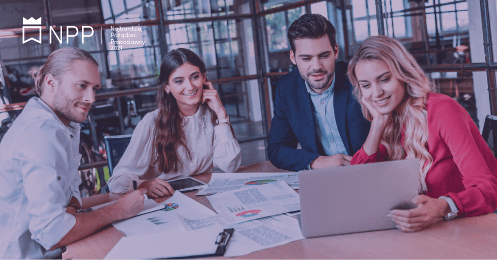 Zdjęcie jest ilustracją do artykułu i przedstawia grupę pracowników siedzących przy stole konferencyjnym i patrzących na ekran laptopa. Na stole leżą wydruki