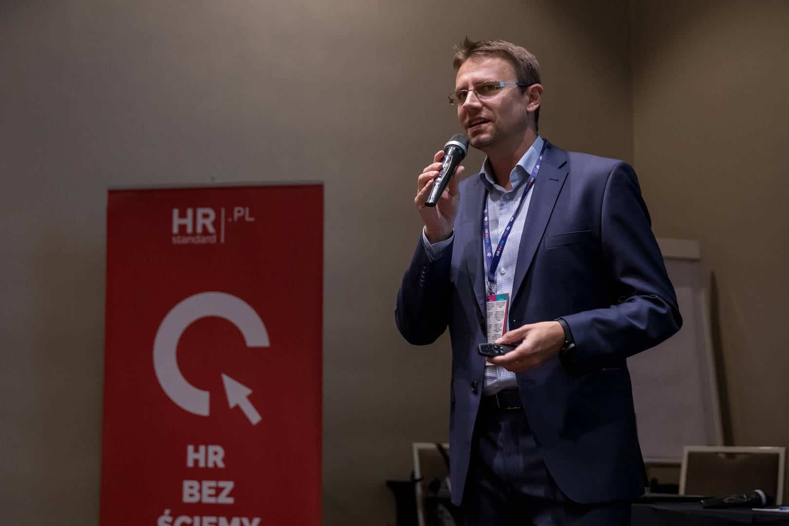 Zdjęcie ilustruje artykuł: X edycja HRcamp za nami! Przedstawia mężczyznę z mikrofonem podczas publicznego wystąpienia.