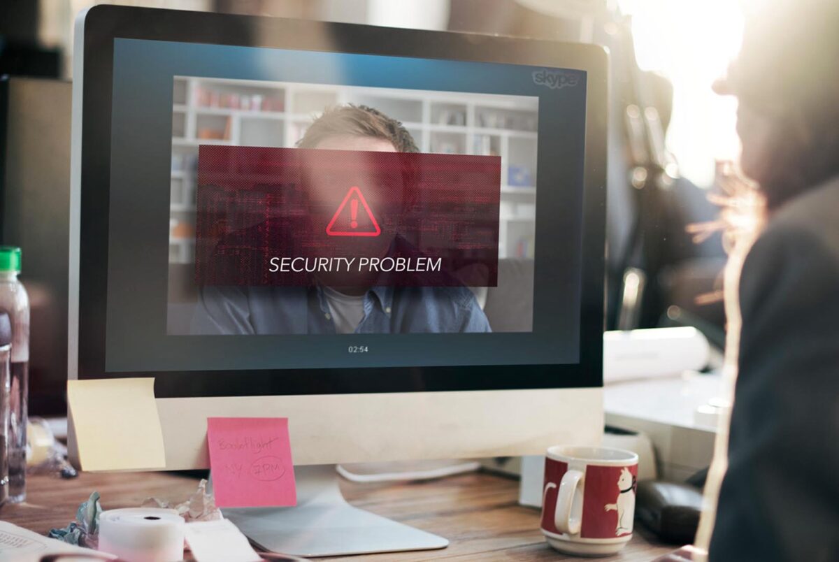 Zdjęcie jest ilustracją do artykułu: Rekrutacja zdalna a ochrona danych osobowych kandydata – na co zwrócić uwagę? Przedstawia rozmowę video dwóch osób. Na ekranie komputera widnieje znak ostrzeżenia i napis " Security Problem"