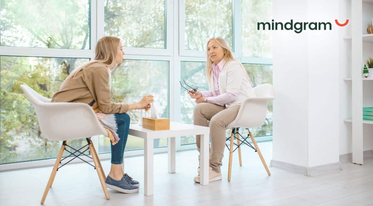 Zdjęcie jest ilustracją do artykułu: Opieka psychologiczna w organizacjach. Czy Twoi pracownicy jej potrzebują? Zdjęcie przedstawia 2 kobiety, jest to rozmowa psycholożki z pacjentką. W górny prawym rogu znajduje się logo: Mindgram.