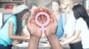 Zdjęcie jest ilustracją artykułu: O jedno słowo czy gest za daleko i żart przestaje śmieszyć. Przedstawia dłonie ludzkie trzymające symboliczny znak kobiecości - symbol planety Wenus. W tle niewyraźne sylwetki kilku kobiet.