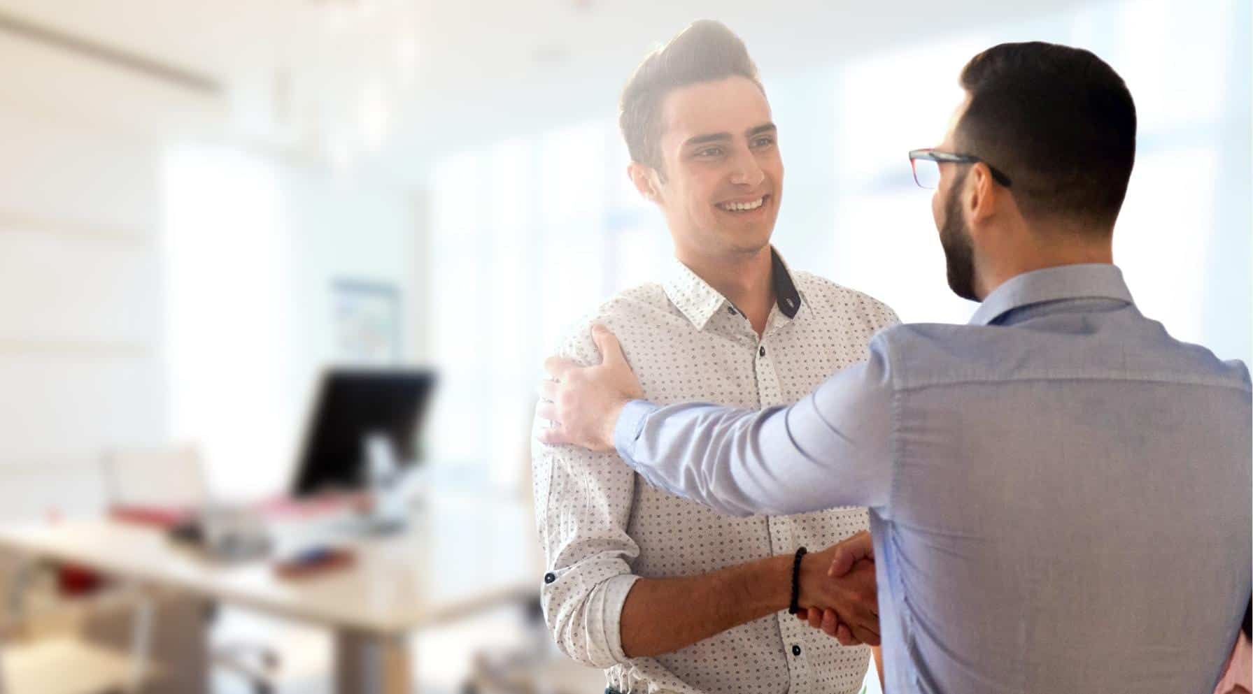 Zdjęcie jest ilustracją do artykułu: Pułapki feedbacku, czyli jak wspierać rozwój nie podcinając skrzydeł. Przedstawia dwóch pracowników ściskających sobie dłonie.