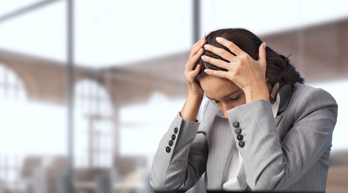Obrazek jest ilustracją do artykułu: Plaga L4. Jak walczyć z wypaleniem zawodowym pracowników?. Przedstawia kobietę w stroju służbowym, która podtrzymuje dłońmi opuszczoną głowę.