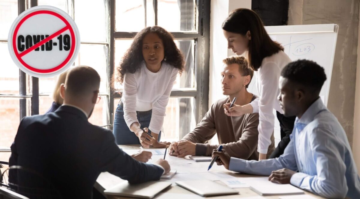 Zdjęcie jest ilustracją do artykułu: Istotne zmiany w prawie pracy. Upłynął ważny termin. Przedstawia pracownikó przy stole konferencyjnym oraz przekreślony znak COVID-19.